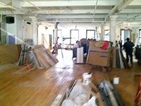 Indoor space under renovation with wood floors and workers visible.