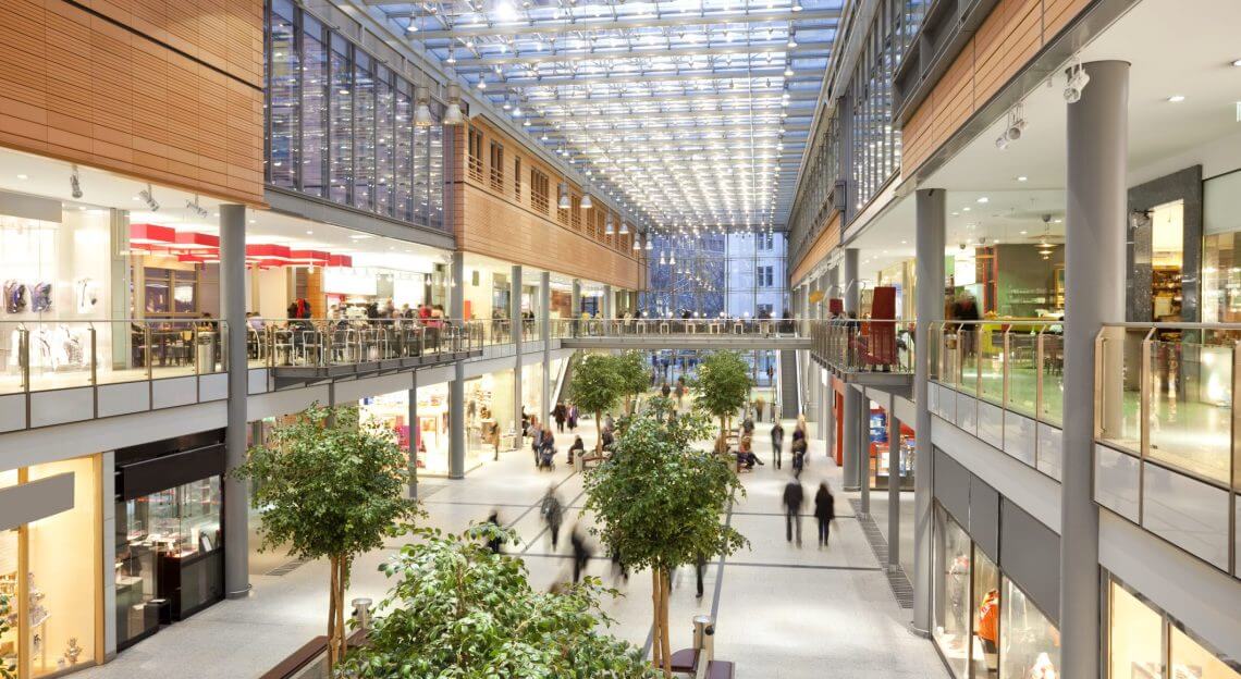 Modern NYC shopping mall with two floors, glass ceiling, and a few people shopping.