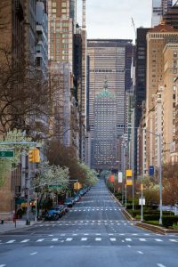 Empty city street of Park Avenue with skyscrapers on either side and parked cars along the curb