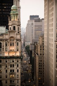 Bustling scene on Wall Street, skyscrapers on either side and cars driving down the street