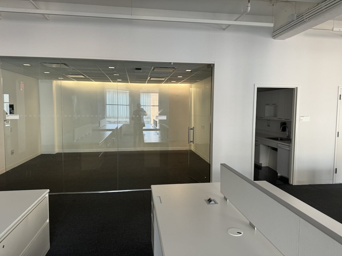 Empty office space with white walls, dark carpet, and glass-walled conference room.