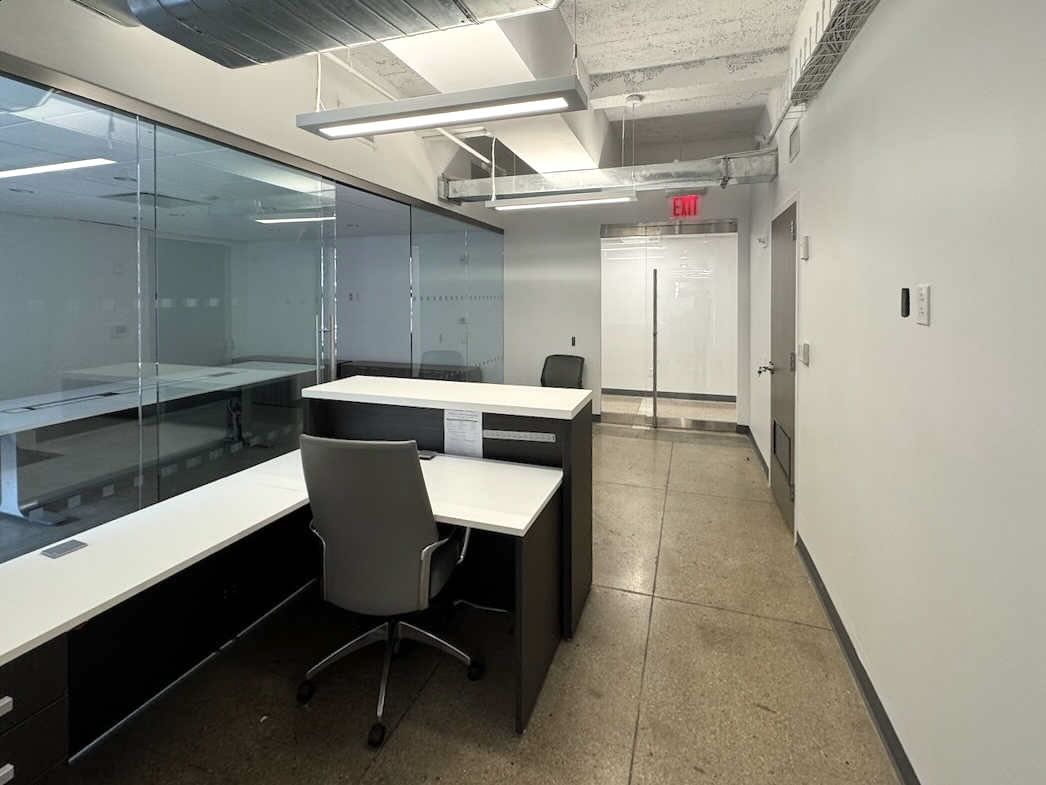 Modern office with gray walls, glass partition, desk, and ceiling ducts.
