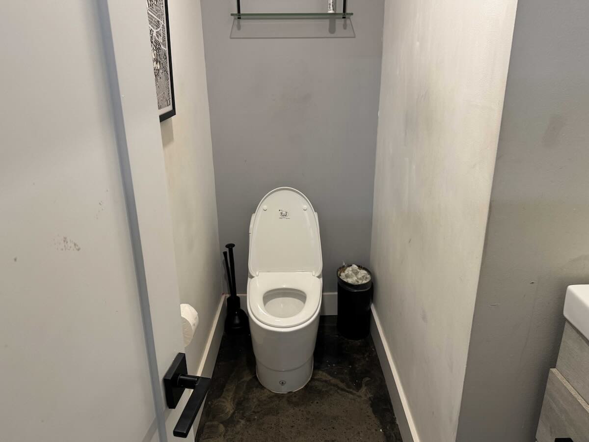 Small bathroom with white toilet, gray wall, and framed picture.
