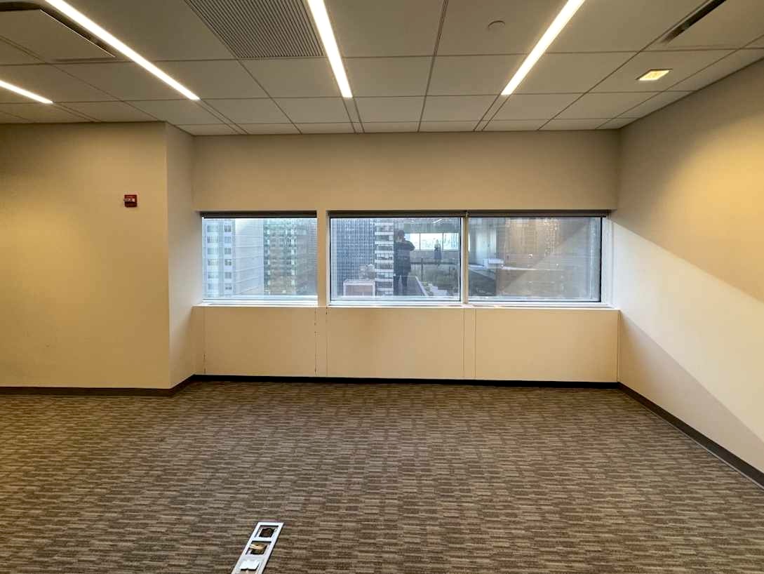 Empty office with beige carpet, white walls, and large windows.