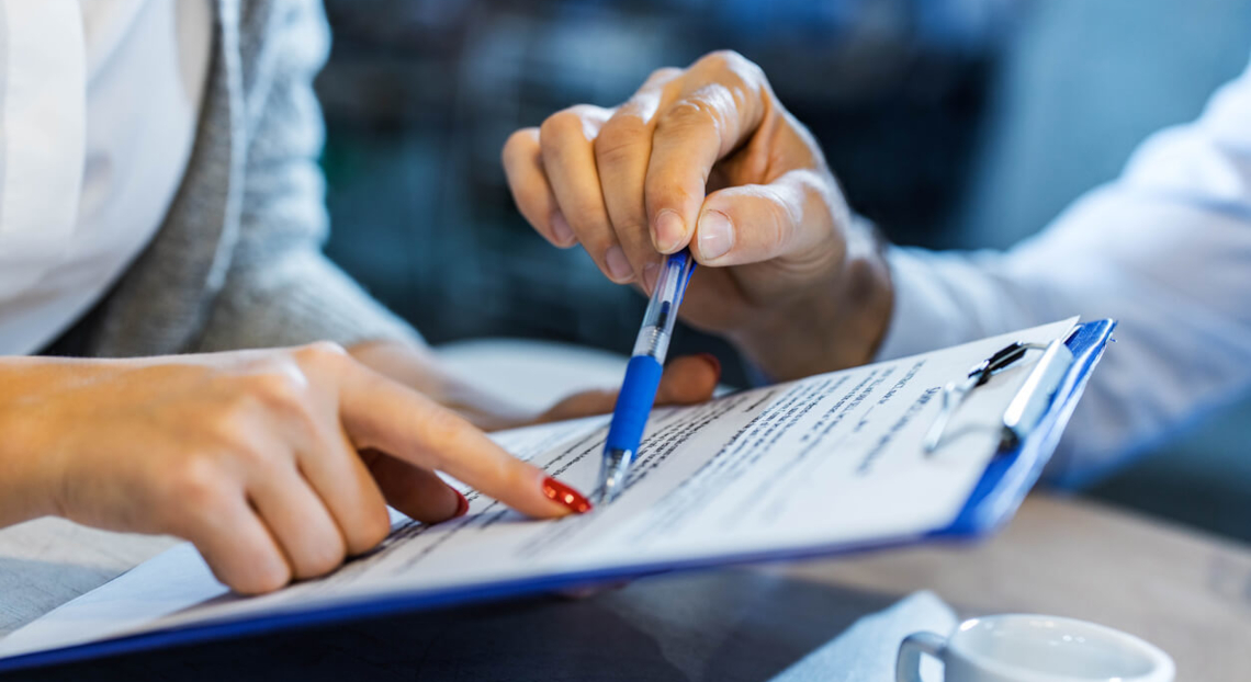 Two people review lease offer with blue pen and pointing finger.