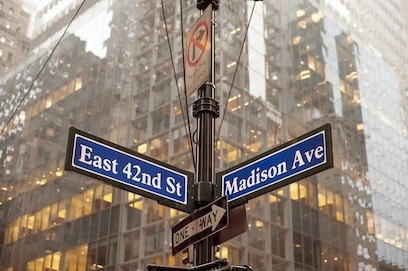 East 42nd St and Madison Ave street signs with city reflections.