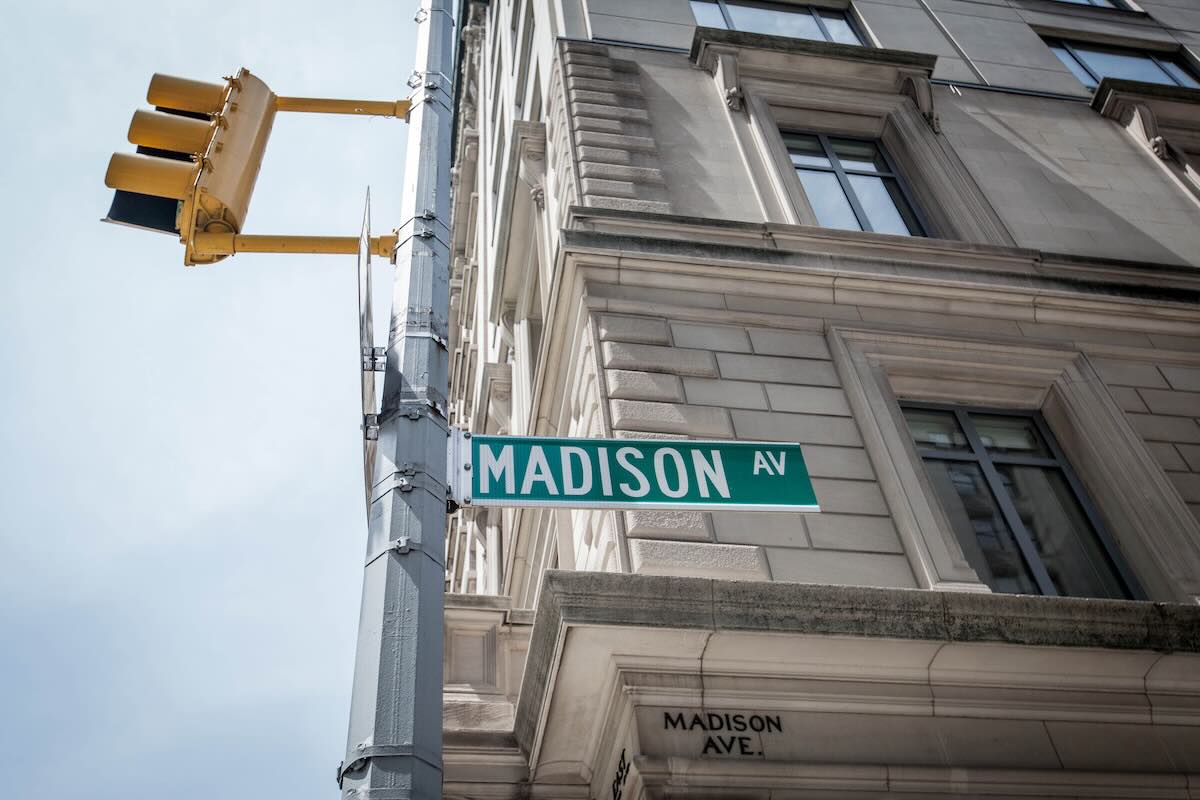 Madison Ave street sign with traffic light on ornate building.