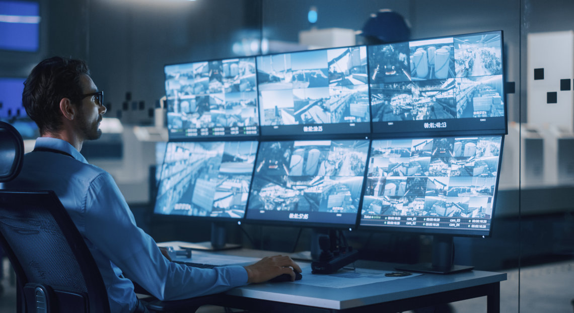 Person watches security camera feeds on screens in NYC office.