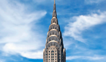 Chrysler Building spire with metallic arches against blue sky.