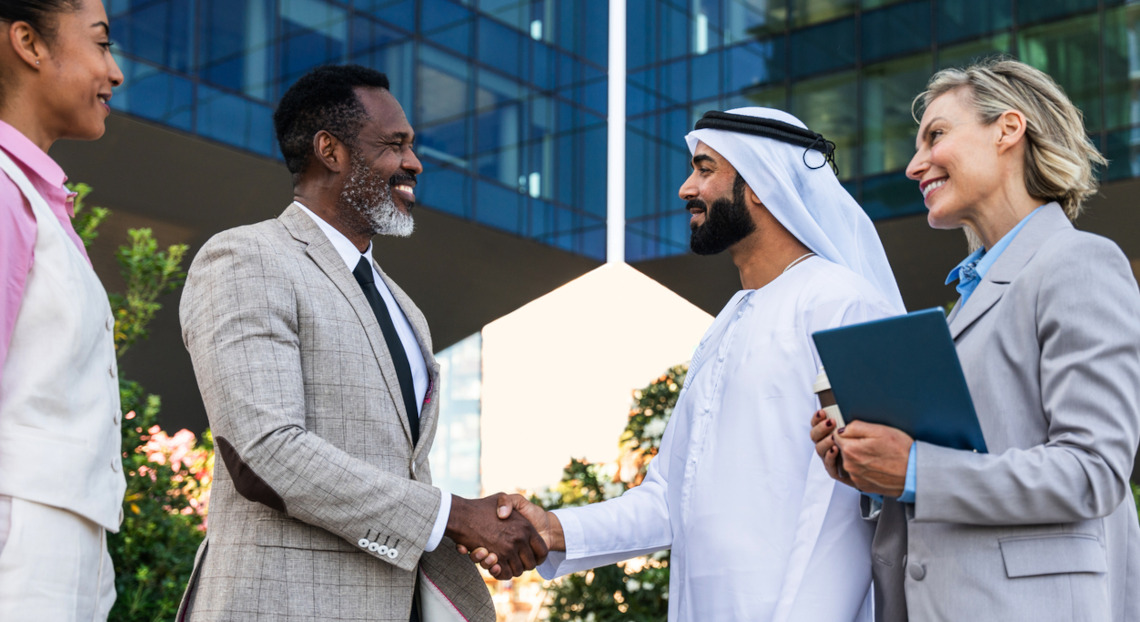 Businesspeople, including gulf investor, shake hands outdoors.