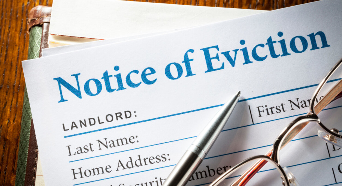 Eviction notice form with pen and eyeglasses on wood surface, close-up.